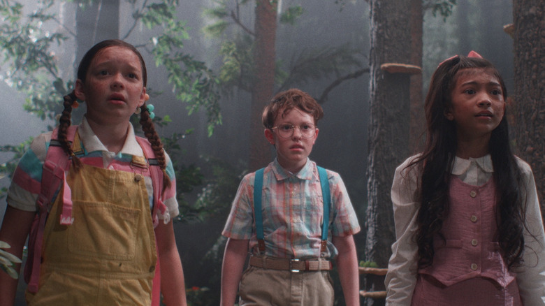 Freddy, Oliver, and Hannah stand in the woods with terrified looks on their faces in Buddy