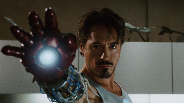 Robert Downey Jr. as Tony Stark/Iron Man in Iron Man, wearing a prototype of his mechanized hand while he raises it toward the camera.