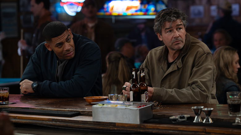 Aaron Pierre as John Stewart and Kyle Chandler as Hal Jordan sitting at a crowded bar in Lanterns