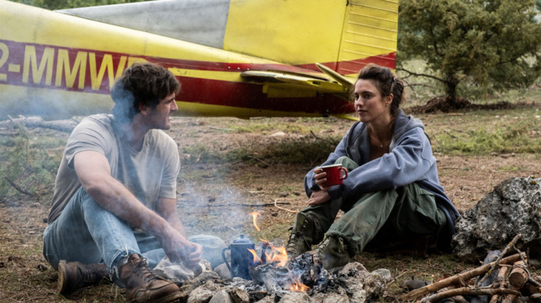 Hig and Cima sit by a fire in front of a plane in The Dog Stars