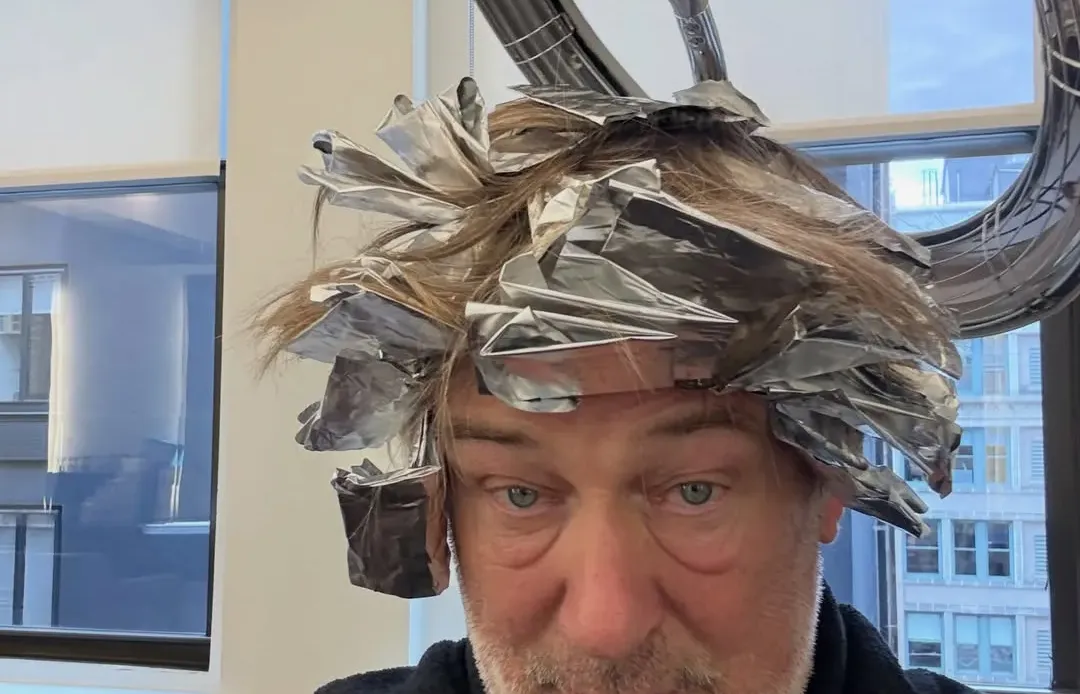 Alec Baldwin with hair in foils under a hair dryer.