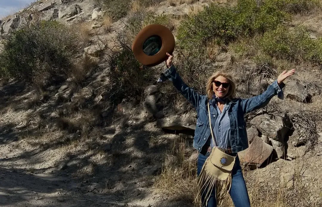 Christie Brinkley raising her cowboy hat in a Montana landscape.