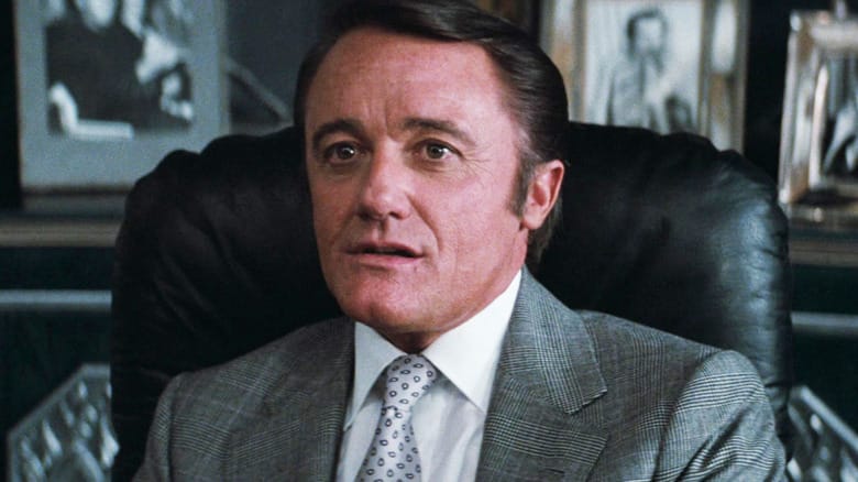 Robert Vaughn's Ross Webster sits at his desk in Superman III