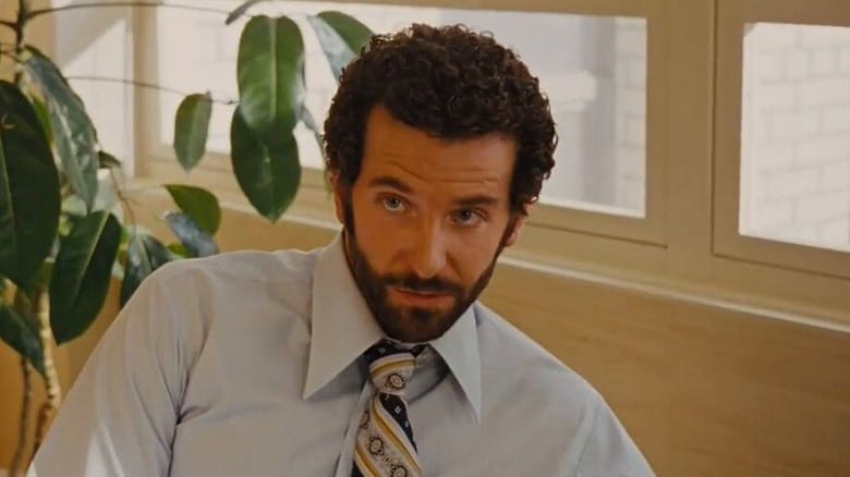 Bradley Cooper as Richie DiMaso sitting down in front of a plant in American Hustle