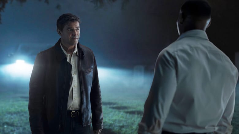 Kyle Chandler's Hal Jordan sits opposite Aaron Pierre's John Stewart stand opposite one another in a graveyard in front of a parked car in Lanterns