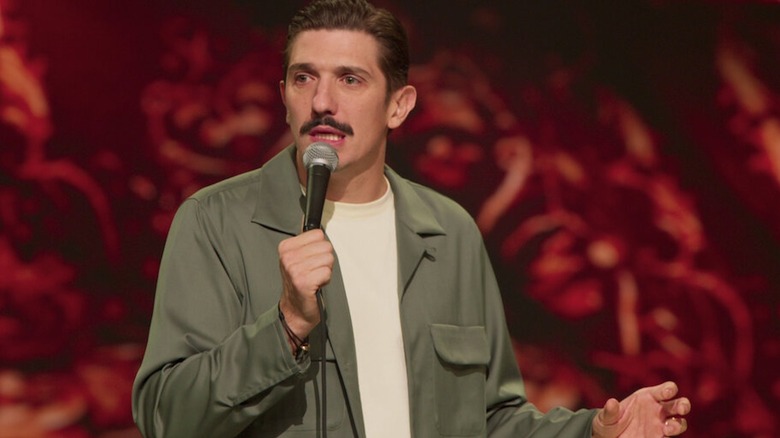 Andrew Schulz holds a microphone on stage in his stand-up special Life