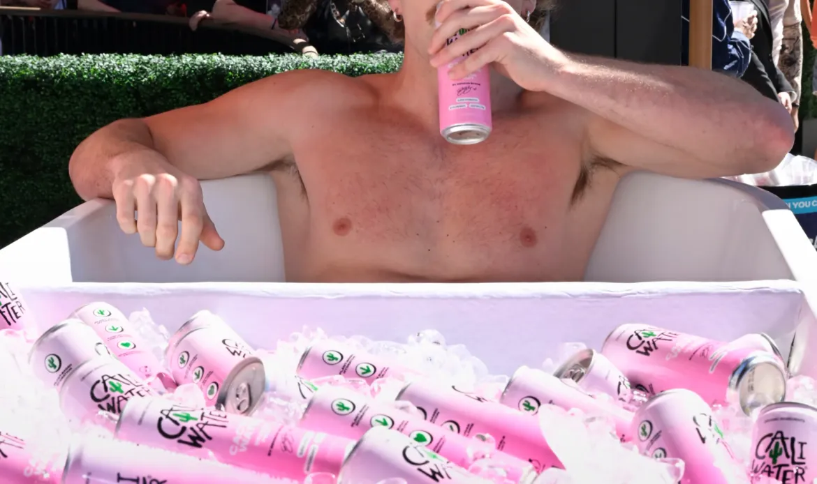 Benson Boone drinks a Caliwater can while sitting in a bathtub filled with ice and more Caliwater cans.