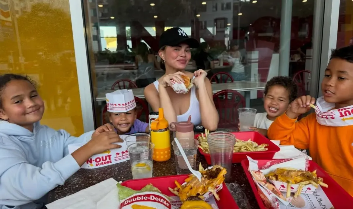 Chrissy Teigen sits at a restaurant table with her children, enjoying In-N-Out burgers and fries.