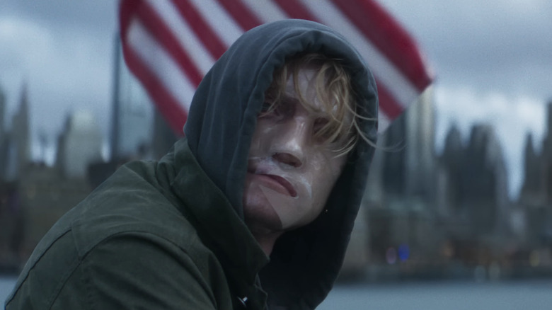 Tom Rhys Harries' Matt Hagen/Clayface sitting by a river in front of a US flag in Clayface