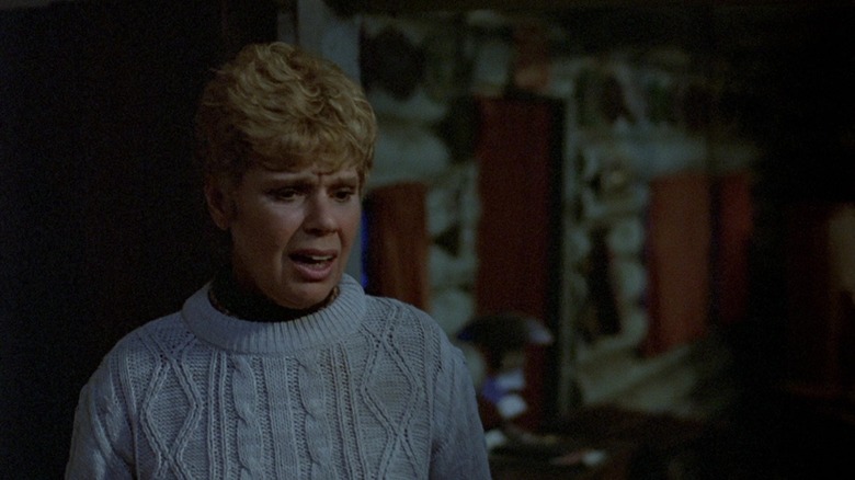 Betsy Palmer as Pamela Voorhees standing in the cabin in her blue sweater in Friday the 13th (1980).