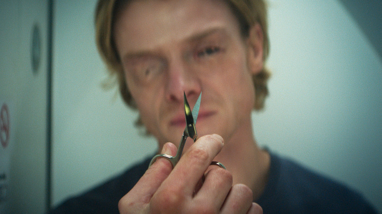 Matt Hagen holding some scissors while looking at himself in a mirror in Clayface