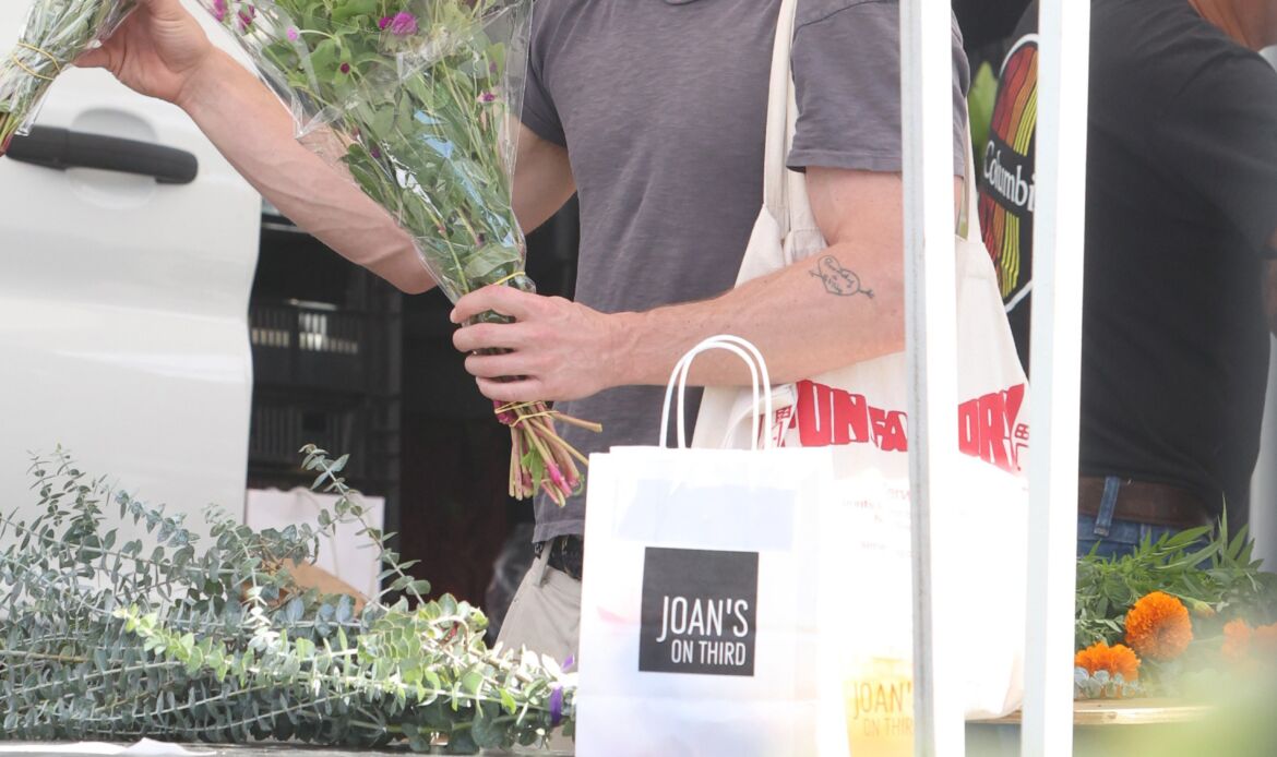 Jeremy Allen White holds a bouquet of flowers at a farmers market.