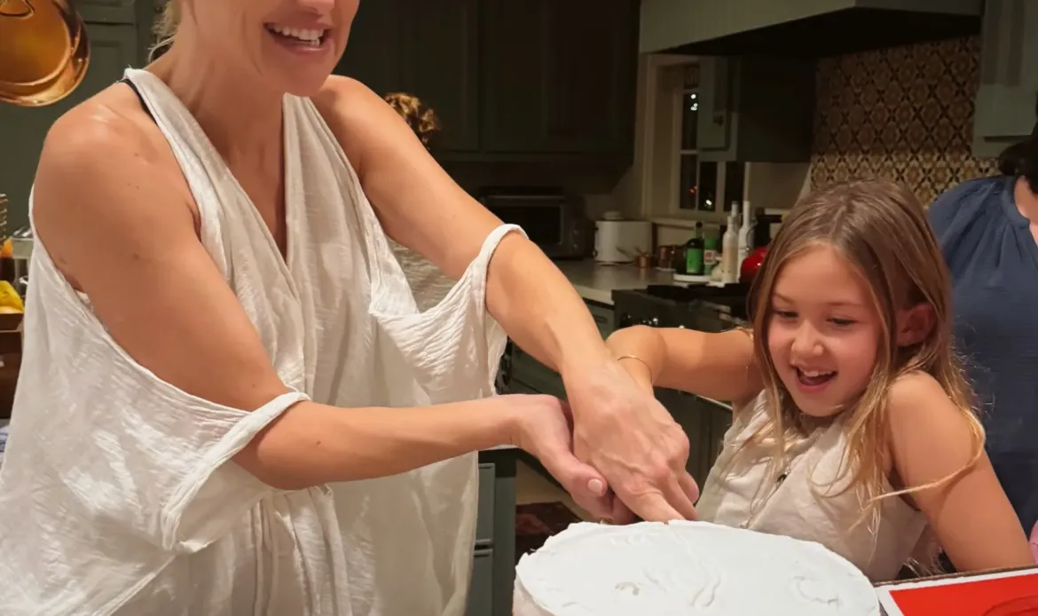 Kate Hudson wearing a party hat and a young girl smiling as they cut a birthday cake together.