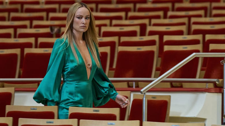 Olivia Wilde as Carol Spedding wearing a green dress and walking through an empty theater in Behemoth!