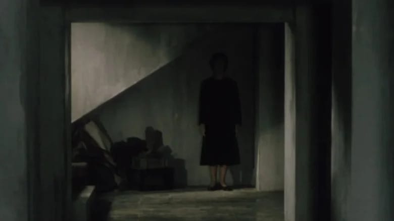 A ghostly woman stands in the shadows under a staircase in Pulse (2001)