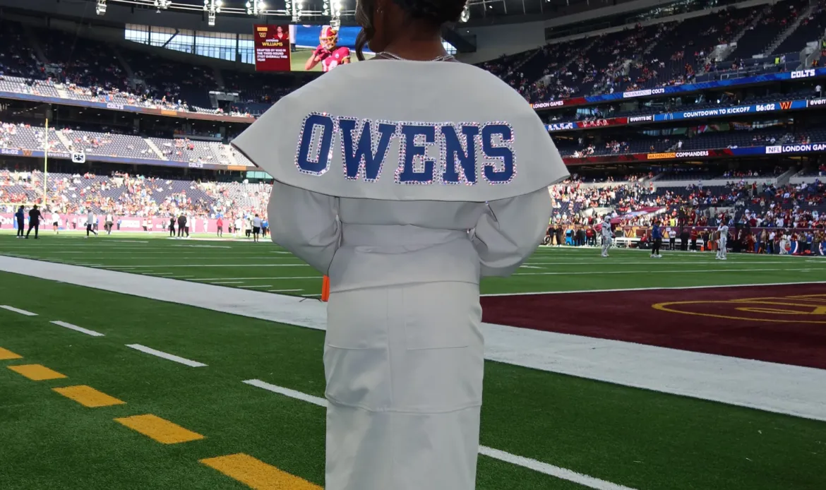 Simone Biles stands on a football field wearing a custom white outfit with the last name Owens and number 38 spelled out in crystals on the back.