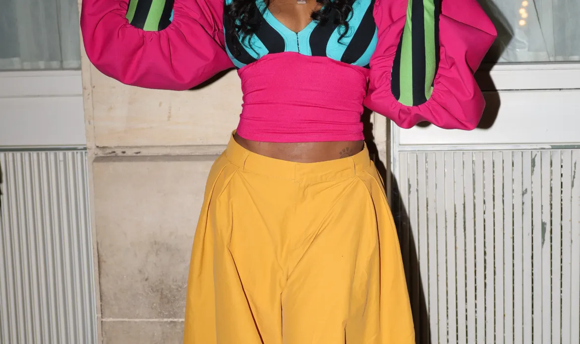 SZA wears a colorful outfit featuring puffed sleeves, a striped bodice, a yellow midi skirt, and a metallic hat outside Siena restaurant.