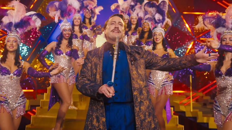 Caesar Flickerman hosting a glitzy show with showgirls in The Hunger Games: Sunrise on the Reaping