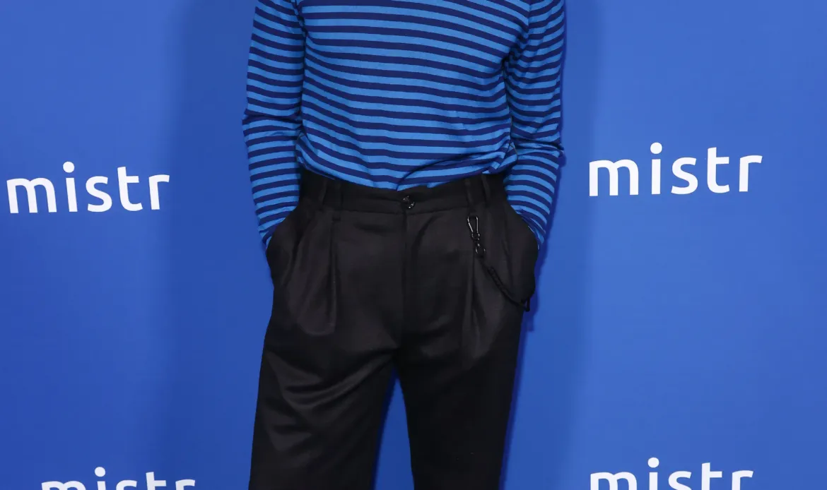 Cheyenne Jackson poses on the blue carpet in front of a step-and-repeat backdrop featuring the MISTR logo.